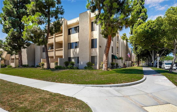 Front view of a multi-story apartment building with balconies and surrounded by trees.