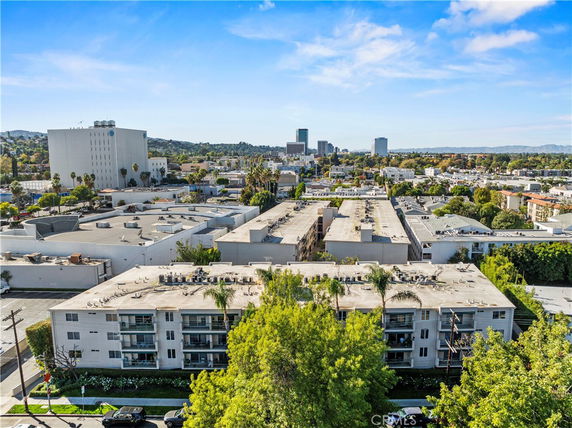 Aerial view of a cityscape with multiple buildings, including a prominent multi-story structure in the foreground and distant skyscrapers.