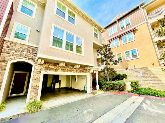 Front view of a multi-story residential building with stone and stucco facade, featuring a garage and entrance.