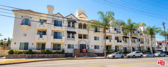 Front view of a multi-story apartment building with balconies and palm trees.