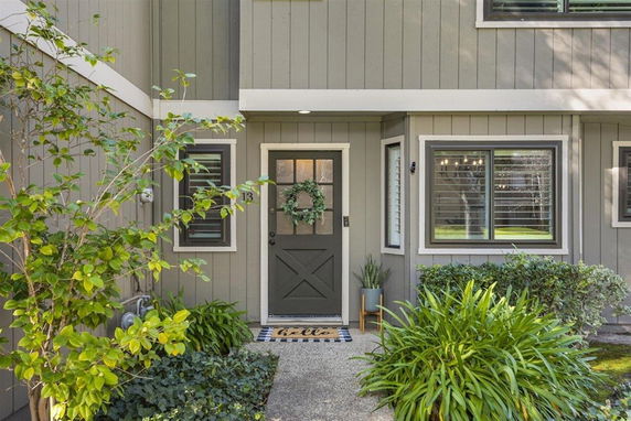 Front view of a house with a green door and windows, surrounded by plants.