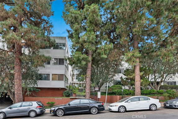 Front view of a multi-story residential building partially obscured by tall trees.