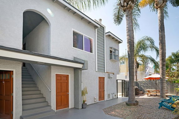 Front view of a two-story building with exterior stairs leading to the upper level and palm trees in the surrounding area.