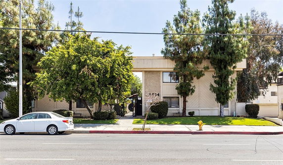 Front view of a two-story apartment building with trees and a white car parked in front.
