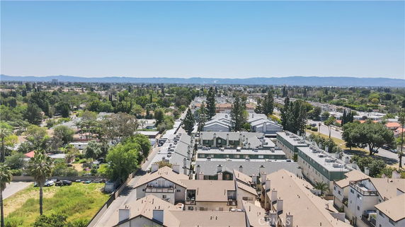 Aerial view of residential buildings with surrounding greenery and distant hills.
