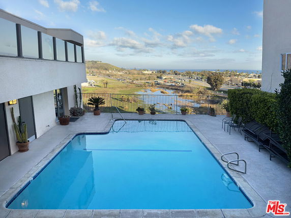 Outdoor area with a swimming pool next to a modern building, overlooking a scenic view.
