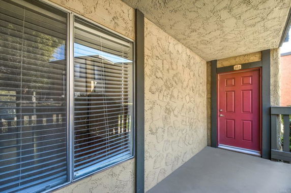 Front view of a building entrance with a red door and a window with blinds.