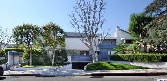 Front view of a multi-story house with a driveway and surrounding greenery.