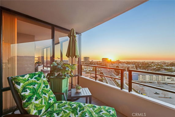 Balcony with outdoor furniture overlooking a cityscape during sunset.