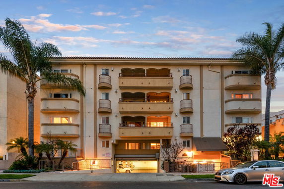 Front view of a multi-story apartment building with balconies and ground-level parking.