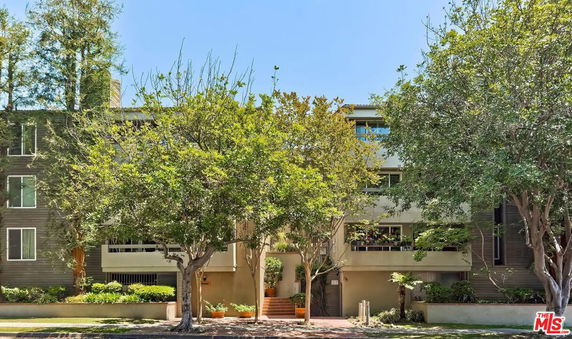 Front view of a multi-story residential building with balconies and surrounded by trees.