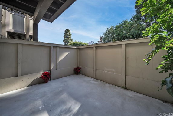 An enclosed outdoor patio area with a concrete floor and high walls, with some potted plants and a glimpse of trees above the walls.
