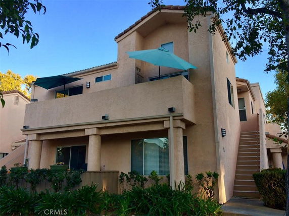Front view of a multi-story house with balconies and outdoor umbrellas.