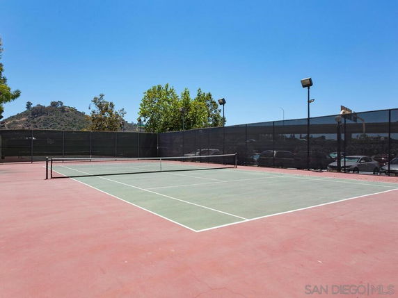 Outdoor tennis court with surrounding lights and fencing.