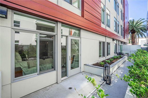 Ground-level outdoor view of a modern multi-story building with large windows and patio area.
