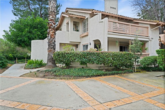 Front view of a two-story house with a balcony and surrounded by greenery.