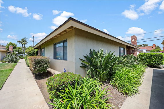 Front view of a single-story house with a brick chimney and surrounded by shrubs and plants.
