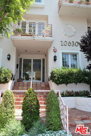 Front view of a multi-story building with a staircase leading to a glass door entrance and balconies with plants.