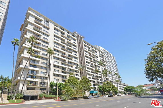 Front view of a multi-story apartment building with balconies and palm trees.