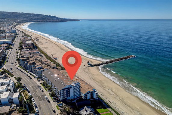 Aerial view of beachfront buildings along a coastline with a long pier extending into the ocean.