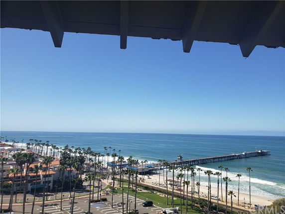 Panoramic view of the ocean, beach, and pier with palm trees and coastal buildings.