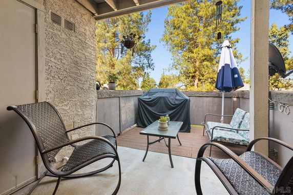 Outdoor patio area with seating, a table, grill, and umbrella, surrounded by trees.