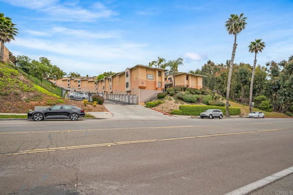 Front view of a multi-story apartment complex with a driveway leading up from the street.