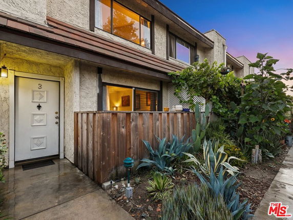 Front view of a two-story house with a small garden and wooden fence.