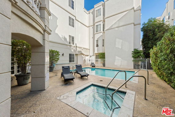 Outdoor swimming pool area with lounge chairs and hot tub in a residential building.