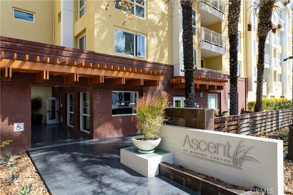 Front view of a multi-story building with a wooden pergola and signage at the entrance.