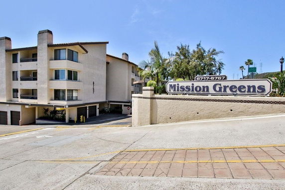 Front view of a multi-story residential building with a sign reading 'Mission Greens.'