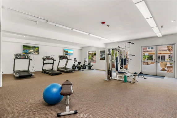 Room equipped with gym equipment including treadmills, exercise bikes, and weight machines.