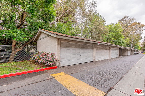 Covered outdoor parking area with garage doors along a paved driveway.