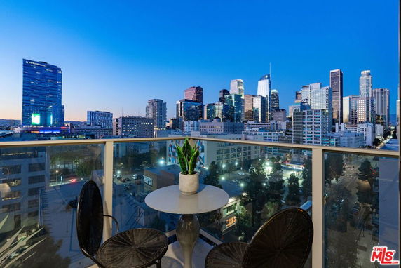 Panoramic city view from a balcony with table and chairs overlooking downtown skyscrapers.