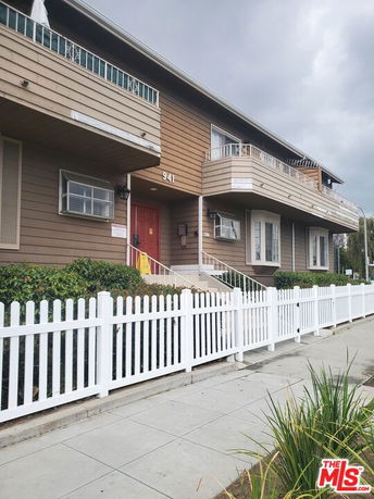 Front view of a two-story building with balconies and a white picket fence.