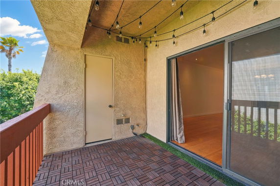 Balcony with string lights and a sliding glass door overlooking green foliage.