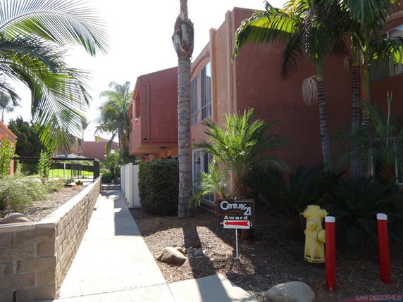 Front view of a multi-story apartment building with a walkway and palm trees.