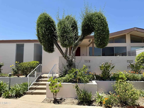 Front view of a single-story house with large windows and a landscaped garden.