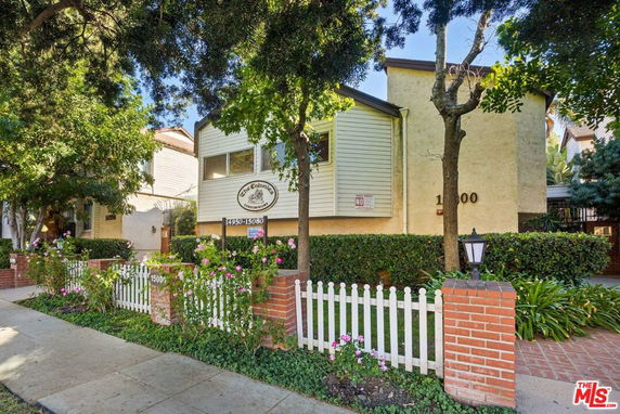 Front view of a multi-story building with a picket fence and greenery.