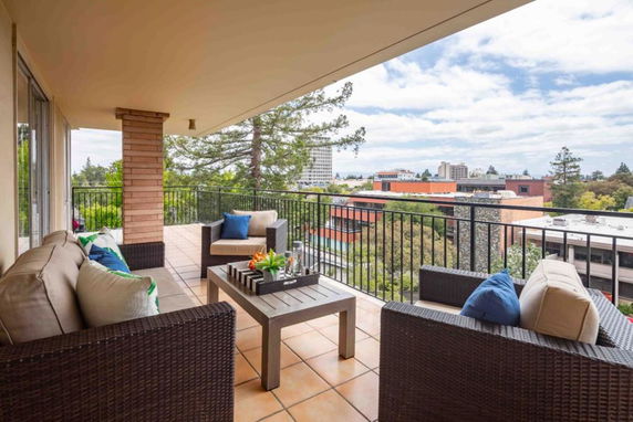Panoramic view from a balcony with outdoor seating overlooking surrounding buildings and trees.
