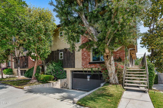 Front view of a multi-story building with brick and wood exterior, featuring a gated entry and outdoor staircase.