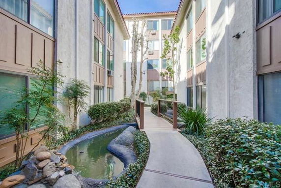 Outdoor view of a pathway between two multi-story buildings with a small stream and landscaping.