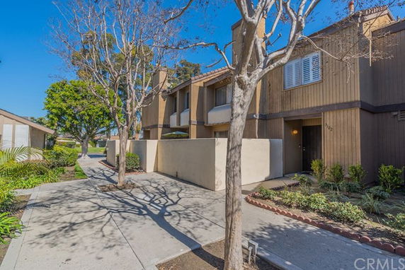 Front view of a two-story townhouse with wooden siding and a small garden area.