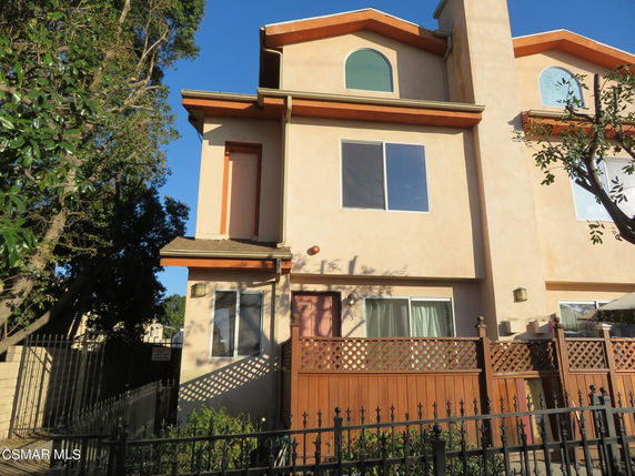Front view of a multi-story house with arched windows and wooden fencing.