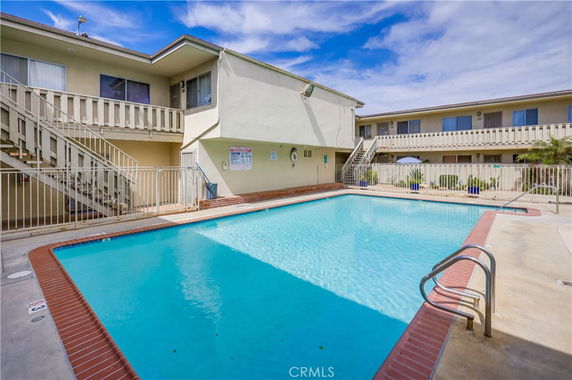 Image of a swimming pool surrounded by a two-story residential building with exterior stairs and balconies.