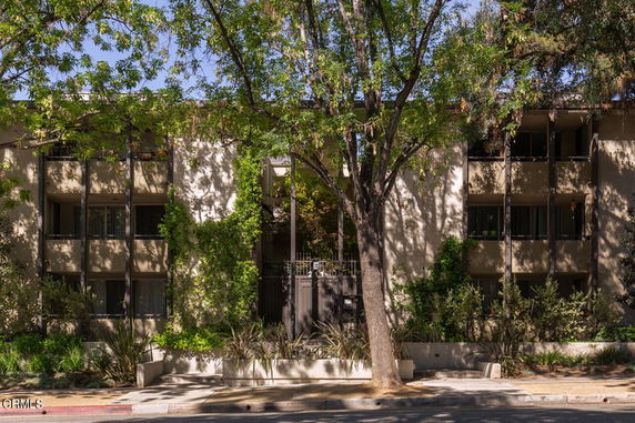 Front view of a multi-story residential building with balconies and large trees in front.