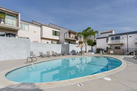 Outdoor swimming pool area with lounge chairs and residential buildings in the background.