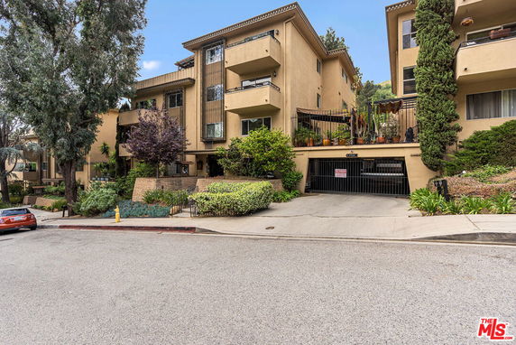 Front view of a multi-story apartment building with balconies and a gated parking area.