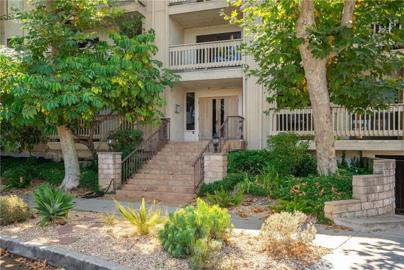 Front view of a multi-story building with a central entrance and surrounding vegetation.