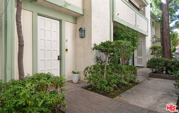 Front view of a two-story building entrance with a white door and surrounding greenery.
